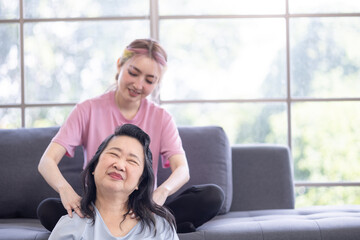 Young Asian daughter massages shoulder, relieves pain of elderly Asian mother at home