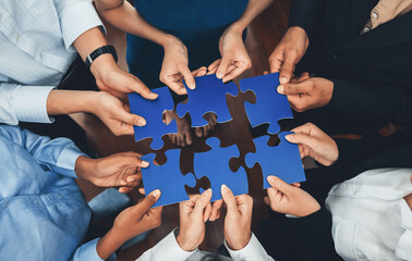 Diverse corporate officer workers collaborate in office, connecting puzzle pieces to represent...