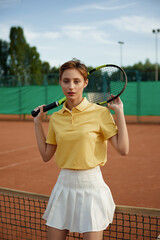 Young woman tennis player in trendy fashion sportswear posing with racket