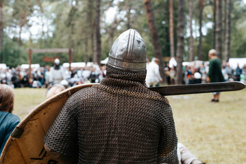 Knight in armor, helmet and sword outdoors, back view