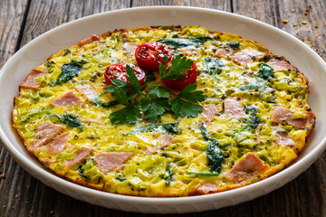Delicious breakfast - egg omelette with mortadella, leek,spinach and cherry tomatoes on wooden table
