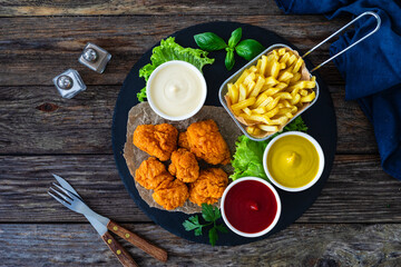 Seared breaded chicken nuggets with French fries on wooden table
