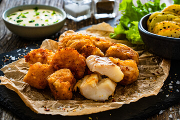 Bakaliaros - seared cod fritters with fried potatoes and fresh vegetables on wooden table 