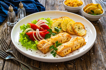 Seared cod loin with fried potatoes and fresh vegetables on wooden table
