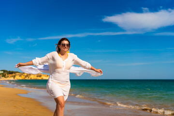 Beautiful woman walking on sunny beach holding shawl