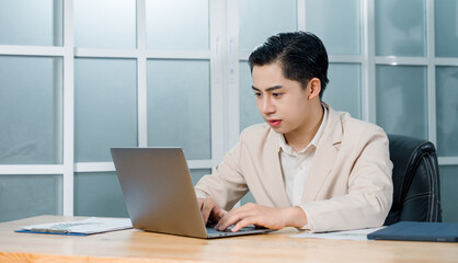Fototapeta premium Businessman in a light blazer smiles and celebrates in front of his laptop, conveying excitement and success in a professional setting.