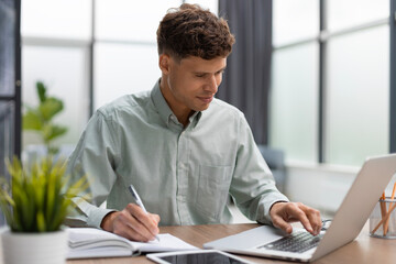 Fototapeta premium Young modern business man analyzing data using computer while working in the office.