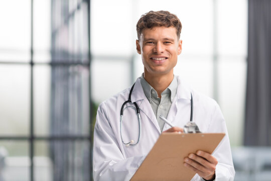 Doctor in white medical uniform with statoscope writing personal file of patient.