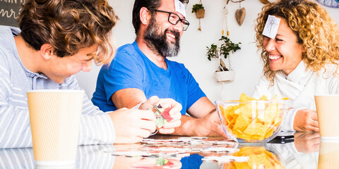 Happy real people family play together with cards at home on the table laughing and having fun. Man and woman father mother with son enjoy time in playful indoor leisure activity on sunday holiday