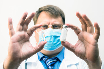 Male doctor in a mask holds an ampoule of a medical drug, close-up.