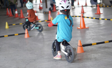 young girls 5 years old races on balance bike in a parking area with cones as track, back view, behind view shoot.