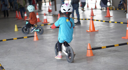 Obraz premium young girls 5 years old races on balance bike in a parking area with cones as track, back view, behind view shoot.