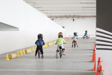 kids from 2-5 years old races on balance bike in a parking area, back view, behind view shoot.