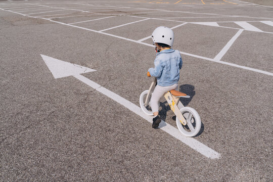 Сaucasian girl preschooler riding wooden balance bike on asphalt road