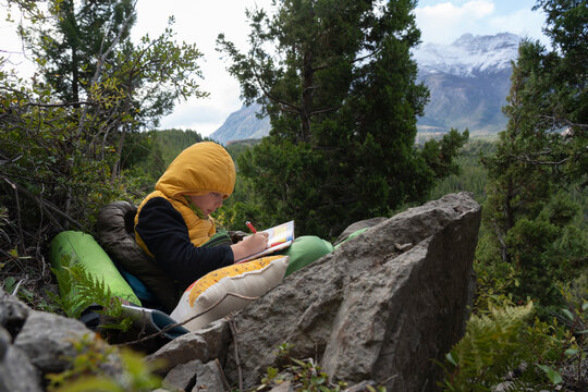 One boy writing on a notebook sitting on rock in the mountains