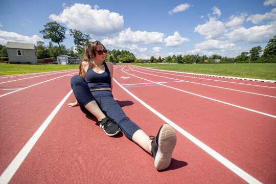 woman sits and relaxes on a running track while working out