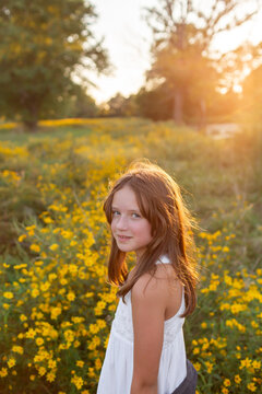 Female child in white dress standing wildflowers at sunset