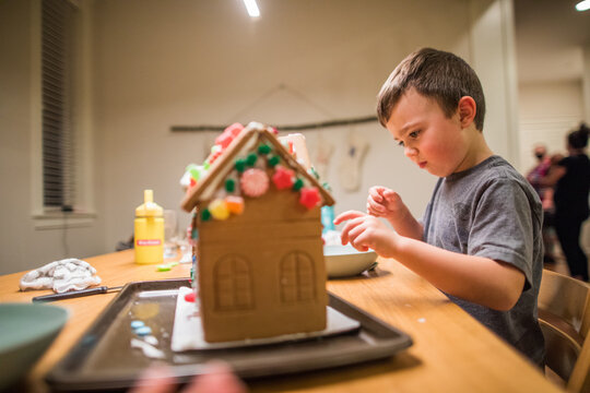 side view of young boy decorating a gingerbread house.