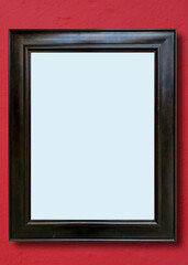An empty black wooden photo or art frame on a burgundy colored wall.