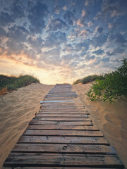 Wooden footpath through the sand leading to the beach. Beautiful morning sky with fluffy clouds