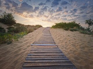 Fototapeta premium Wooden path through the sand leading to the beach. Beautiful morning sky with fluffy clouds
