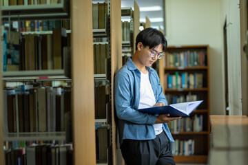 male student doing research by book at library self study, preparing for exams, self study concept