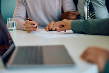 Close up of couple signing agreement with bank manager in office.