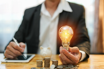 Business man holding light bulb on the Green background nature and writing on note book it for...