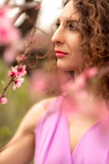 Woman peach blossom. Happy curly woman in pink dress walking in the garden of blossoming peach trees in spring