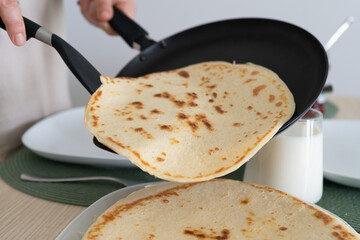 Placing pancakes on a plate after frying them in a pan. Delicious meal preparation, stacking the pancakes on top of each other before serving them at the table.