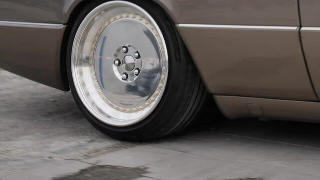 An old car in motion and a close-up of a silver and tuned wheel
