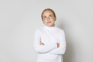 Child with crossed arms looking up on whitestudio wall background. Young girl 10 years old, studio...