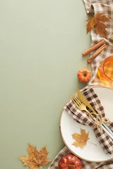  Autumnal table decor idea. Top view vertical shot of plate, cutlery, napkin, tablecloth, glass, cinnamon sticks, pumpkins, autumn leaves on olive background with empty space for advert or text © Goncharuk film