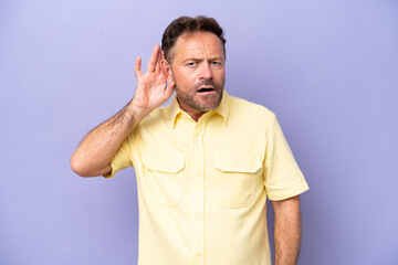 Middle age caucasian man isolated on purple background listening to something by putting hand on the ear