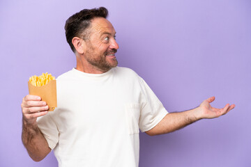 Middle age caucasian man holding fried chips isolated on purple bakcground with surprise expression while looking side