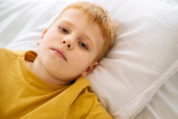 Vibrant red-haired boy exudes charm on a pristine white bed, capturing innocence and warmth