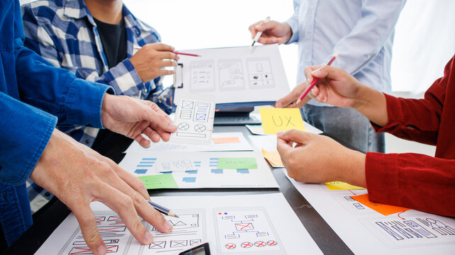 Close-up ux developers and ui designers use augmented reality to brainstorm on mobile app interface wireframe designs on modern office desks. Creative digital development office