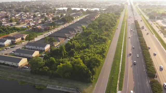 Busy traffic on Interstate 10 highway near Lake Barrington early morning along row of townhouses, condos, lush green trees and residential units in Little Woods, Eastern New Orleans