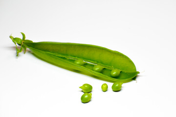 A pod of green peas in close-up. Open doors with round bright green peas. White background. Individual seeds lie next to the pod.