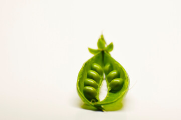 A pod of green peas in close-up. Open doors with round bright green peas. White background.