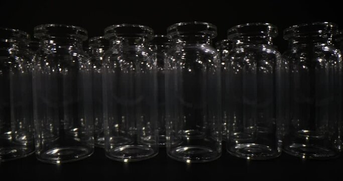 Transparent glass vials designed for vaccines stand in row on dark background. Professional laboratory glassware for medical purposes
