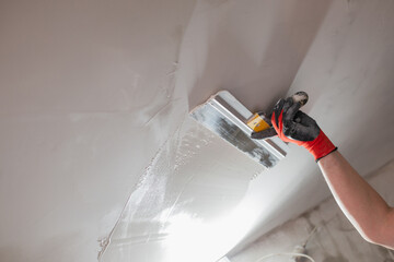 The master hand with a wide spatula applies white putty to the wall - leveling the wall into a...