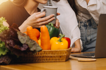 Happy two young women looking laptop computer during cooking together in kitchen room at home. Two young diverse lesbian women spending time together. LGBT and gender identity concept..