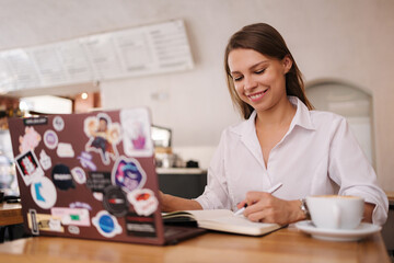 Portrait of female student using laptop in cafe. Lady in formal white shirt smile.