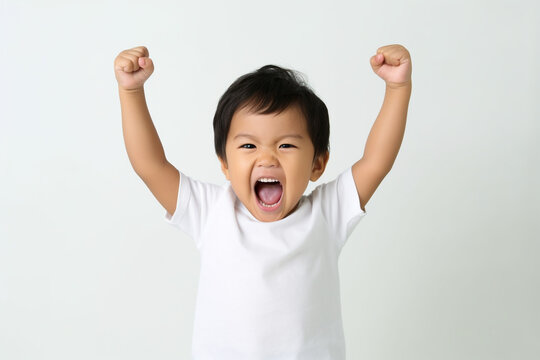 excited Asian toddler boy, just two years old, raises his arms high in the air, donning a white t-shirt, expressing his boundless enthusiasm and infectious happiness isolated white background