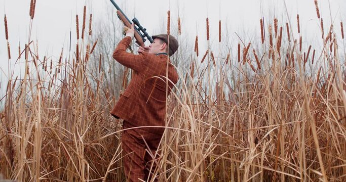 young man shooting into flying duck during hunting in autrumn Slow motion Back rare view, gray dog in foreground. man with a shotgun hiding in reeds near pond, looking up at the sky, watching birds