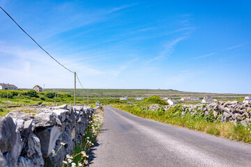Asphalt road with stone walls and power line alongside on a bright sunny day with a blue sky on...