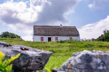 Old traditional irish cottage with a stone fence on a bright sunny day with a cloudy sky