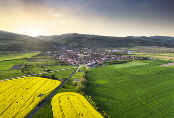 Aerial view of small village with houses placed in green valley with mountain at dramatic sunset,...