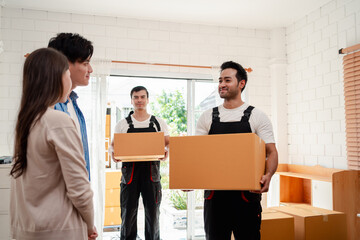 Fototapeta na wymiar Asian Couple check while unloading boxes and furniture from a pickup truck to a new house with service cargo two men movers worker in uniform lifting boxes. concept of Home moving and delivery.